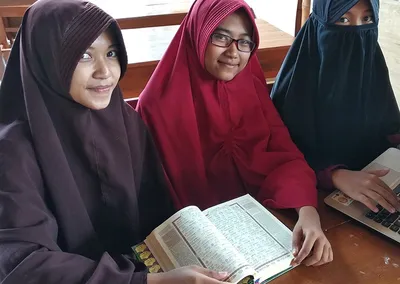 Santriwati tersenyum sambil membuka mushaf Al-Qur’an di meja kelas