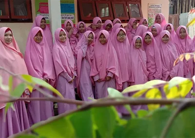Santriwati berfoto bersama di halaman pondok dengan dedaunan di latar depan